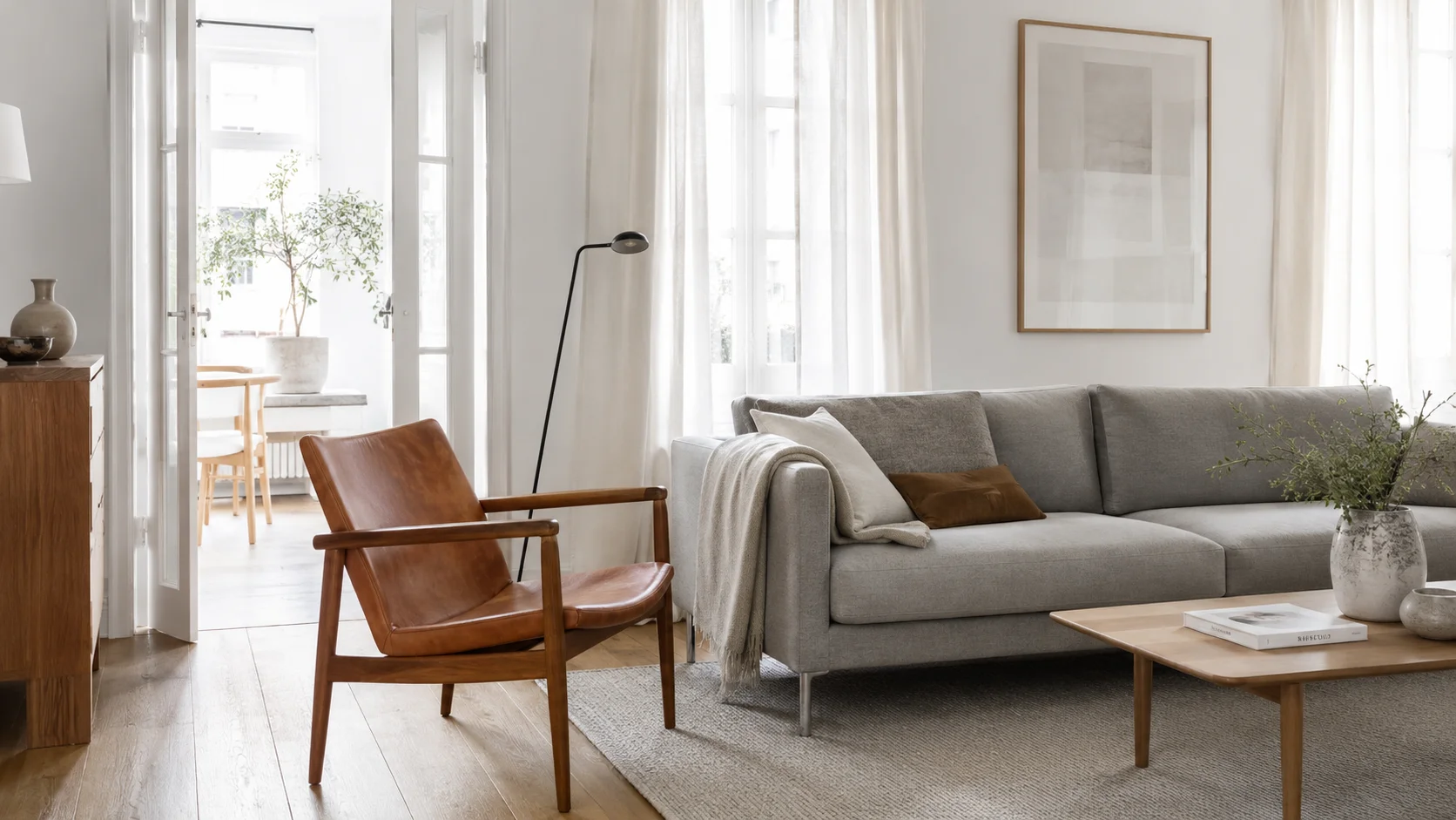 Klassisk dansk lænestol i teak og cognacfarvet læder ved siden af moderne grå sofa i lys stue